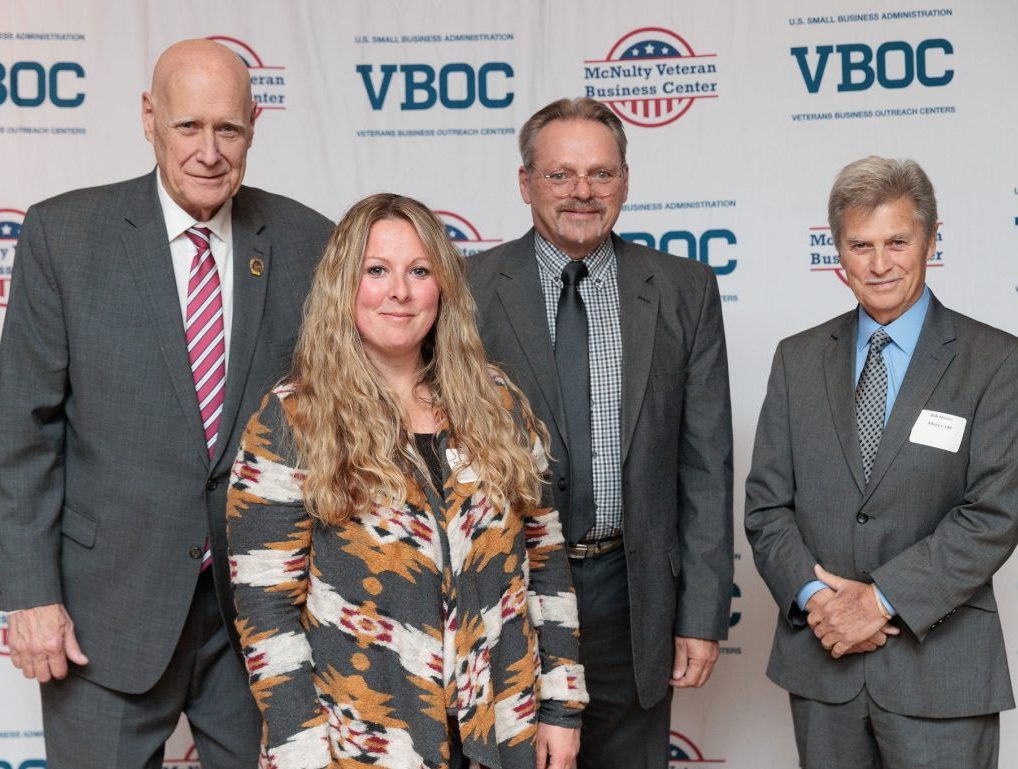 Photo of four people standing in front of a VBOC backdrop